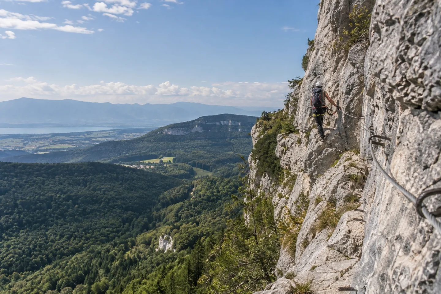 Pratiquant équipé sur une via ferrata au-dessus d’une vallée boisée